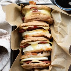 a tray filled with sandwiches covered in melted cheese and bacon on top of brown paper