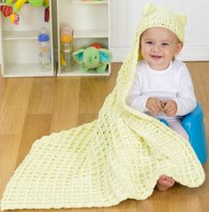 a baby is sitting on the floor under a yellow knitted blanket and smiling at the camera