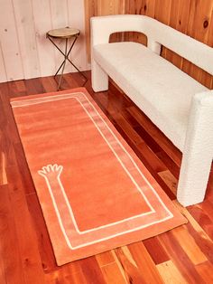 a white bench sitting on top of a hard wood floor next to a red rug