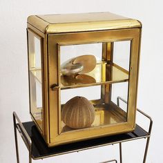 a gold colored display case sitting on top of a metal stand next to a white wall