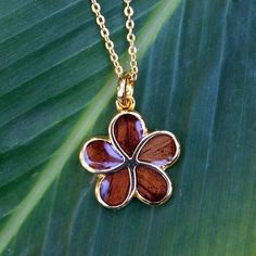 a necklace with a flower on it sitting on top of a green leaf covered ground