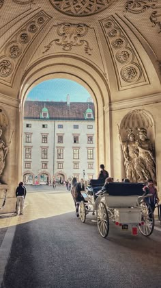 a horse drawn carriage in front of an archway with statues on the sides and people walking around