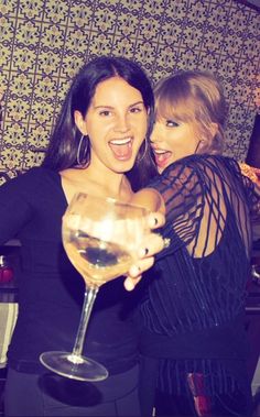 two women standing next to each other holding wine glasses in front of their faces and smiling at the camera