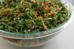 a glass bowl filled with lots of green and orange food items on top of a white table