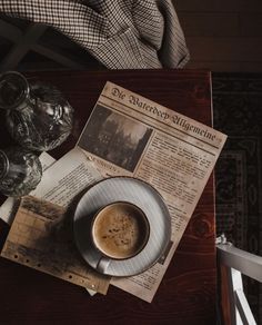 a cup of coffee sitting on top of a table next to a newspaper and glasses