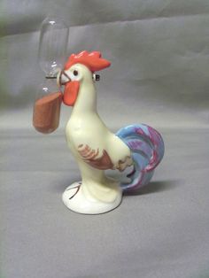 a chicken figurine holding a wine glass in it's beak and looking at the viewer