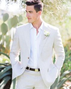 a man in a white suit and flower boutonniere standing next to a cactus