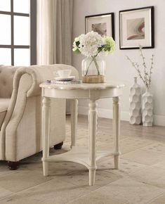 a white table with flowers on it in front of a couch and window sill