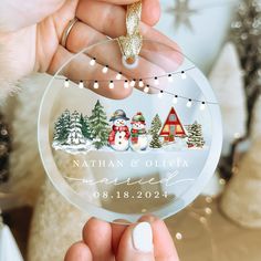 a person holding up a glass ornament with snowmen and houses on it