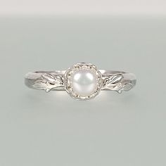 a white pearl sits on top of a silver ring with leaves in the middle and an oval