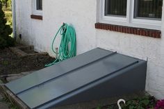 a large metal object sitting in front of a white house next to a garden hose