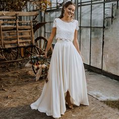 a woman in a white dress standing next to a wheelbarrow with flowers on it