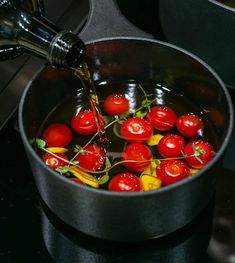 cherry tomatoes are being cooked in a pot on the stove with a ladle full of water