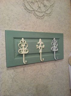 three metal fleur de lis hooks mounted on a green painted wall above a towel rack