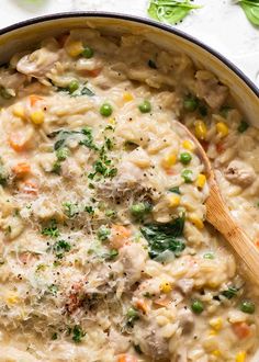 a pot filled with pasta and vegetables on top of a white tablecloth next to a wooden spoon