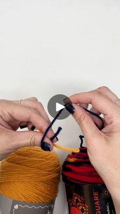 two hands are knitting together yarn on a white surface and another hand is holding the yarn