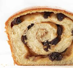 a cinnamon roll with raisins is shown on a white surface, close up