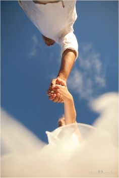 two people holding hands in front of a blue sky with white clouds and the sun shining on them