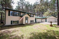 a large house in the woods with green trim and white sidings, surrounded by pine trees