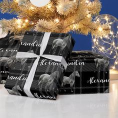 two presents wrapped in black and white wrapping paper under a christmas tree decorated with lights