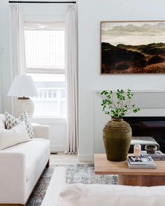 a living room filled with white furniture and a painting on the wall above it's fireplace