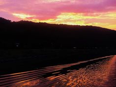 the sun is setting over a river with mountains in the background