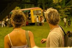 a man and woman standing next to each other in front of a yellow bus on the grass