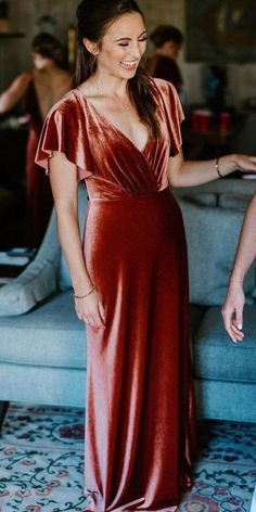 a woman in a red dress is smiling and standing near a couch with her hands on her hips