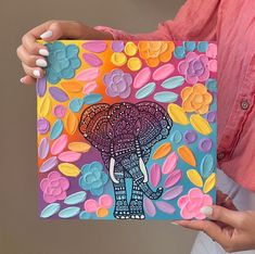 a woman holding up a colorful card with an elephant on it's head and flowers in the background