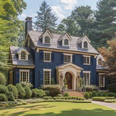 a large blue house with lots of windows and bushes on the front lawn, surrounded by trees