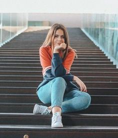 a young woman sitting on top of a metal stair case with her hand under her chin