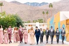 a group of people that are standing in front of some trees and buildings with mountains behind them