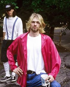 a man sitting on top of a skateboard next to another man with long hair