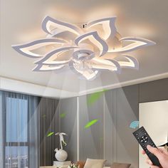 a person holding a remote control up to a ceiling light that is shaped like a flower