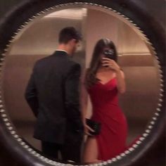 a woman in a red dress is taking a selfie with a man wearing a suit