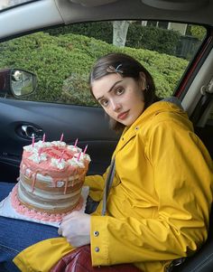 a woman sitting in the back seat of a car holding a cake with candles on it