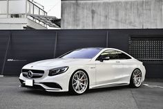 a white mercedes benz coupe parked in front of a black garage door with the doors open