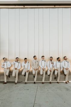 a group of men sitting next to each other in front of a metal wall wearing white shirts and ties