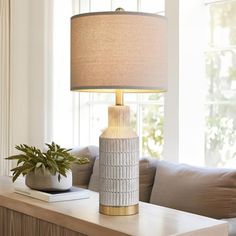 a table lamp sitting on top of a wooden dresser next to a couch and window