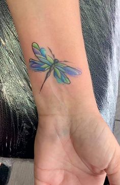 a small blue and green dragonfly tattoo on the left wrist is shown in this image