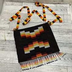 a black and yellow bag with fringes on the bottom is sitting on a wooden floor