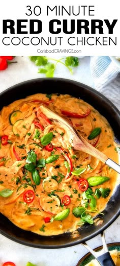 a pan filled with red curry and vegetables on top of a white table next to a spoon