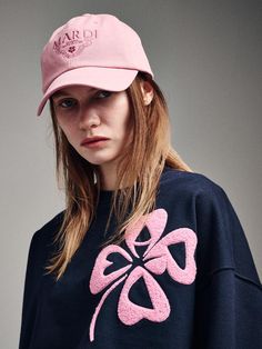 a young woman wearing a pink hat and blue sweatshirt with an embroidered clover on it