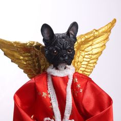 a small black dog wearing a red robe and angel wings on top of it's head