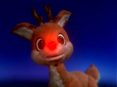 a stuffed animal that looks like a deer with big eyes and red nose, standing in front of a blue background