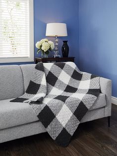 a couch with a blanket on it next to a lamp and window in a blue room