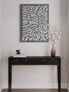 a vase with flowers on top of a black table in front of a white wall