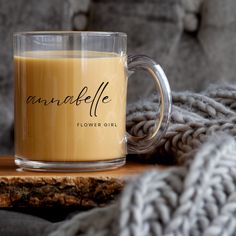 a glass mug sitting on top of a wooden table next to a gray sweater and blanket