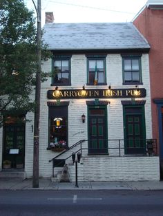 a white brick building with green shutters on the front and stairs leading up to it