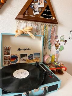 an old record player sitting on top of a suitcase with pictures hanging from the wall behind it